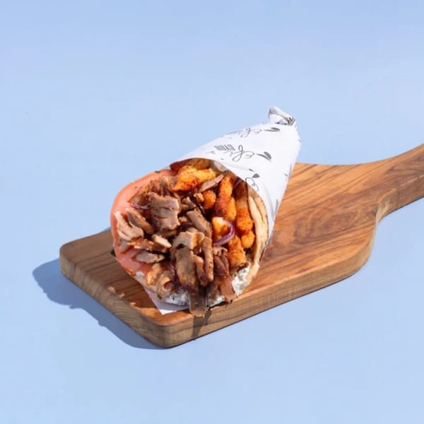 Efi's Gyro with meat, fries, and red onion, wrapped in paper, on a wooden board.