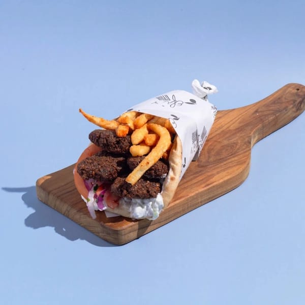 Efi's Gyro with falafel, fries, tzatziki, and vegetables, wrapped in paper on a wooden board.