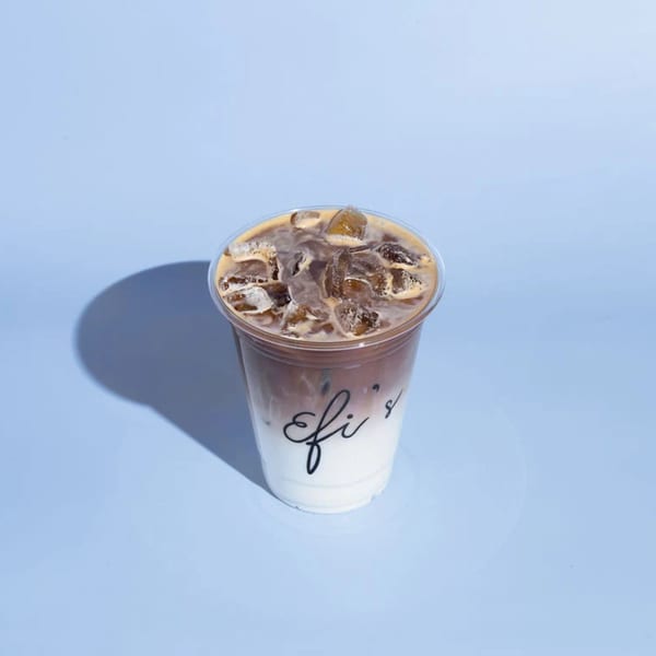 Iced coffee with milk and ice in a clear plastic cup with "Efi's" logo on a blue background.