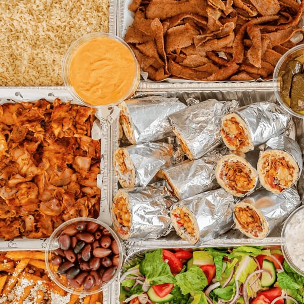 A catering tray filled with various Greek dishes, including gyros, rice, chicken, salad, and olives.