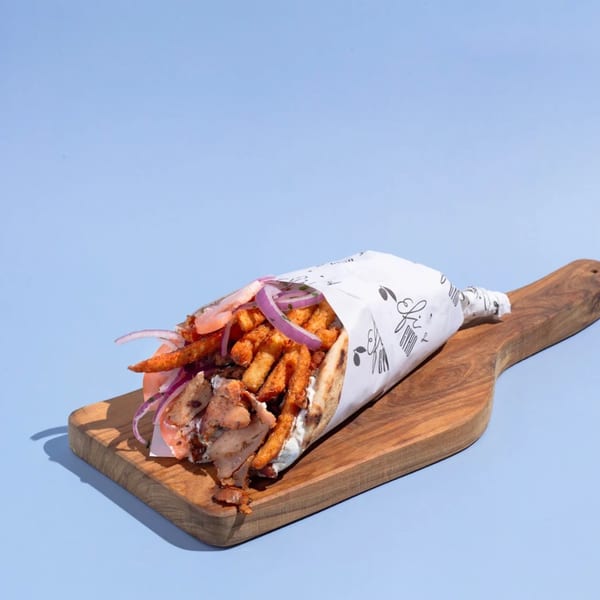 Efi's Gyro with chicken, fries, red onion, and tzatziki, wrapped in paper on a wooden board.