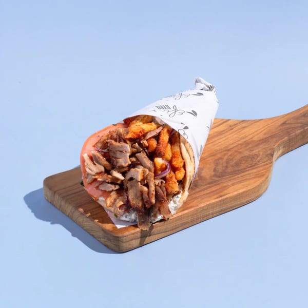 Efi's Gyro, a Greek gyro wrapped in paper, filled with meat and fries, on a wooden board.