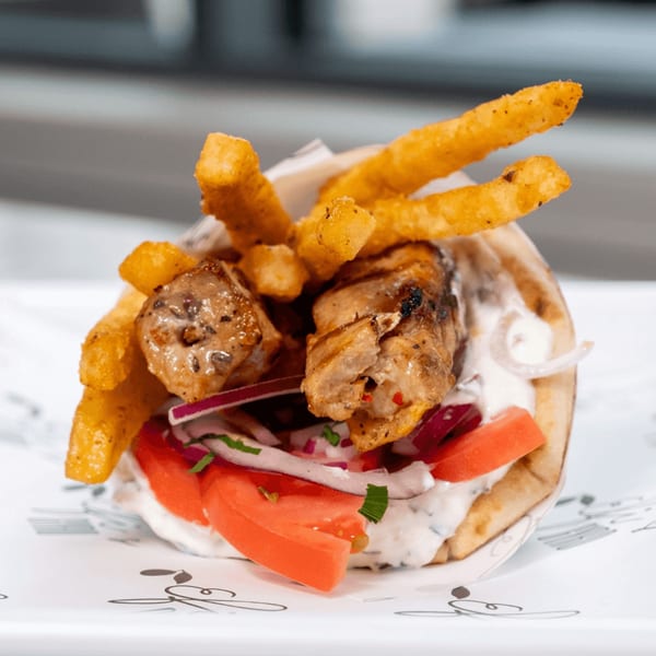 A close-up of a Greek gyro with chicken, fries, tomatoes, onions, and tzatziki sauce.