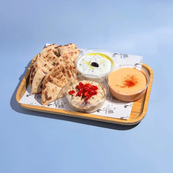 Efi's Gyro pita bread with three dips: tzatziki, hummus, and eggplant salad on a wooden tray.