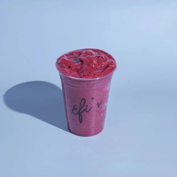 A vibrant red Efi's smoothie in a clear plastic cup, casting a shadow on a light blue background.