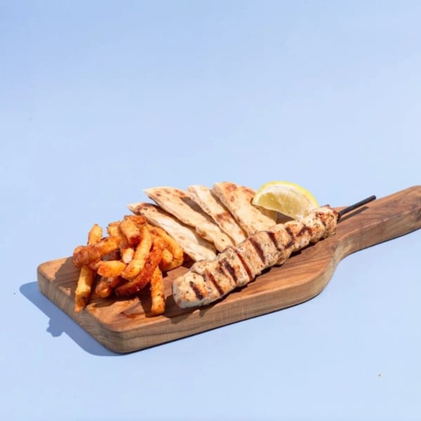 Efi's Gyro chicken skewer with pita bread, fries, and a lemon wedge on a wooden board.