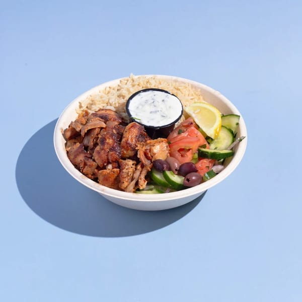 Efi's Gyro bowl with chicken, rice, Greek salad, tzatziki, and lemon on a blue background.