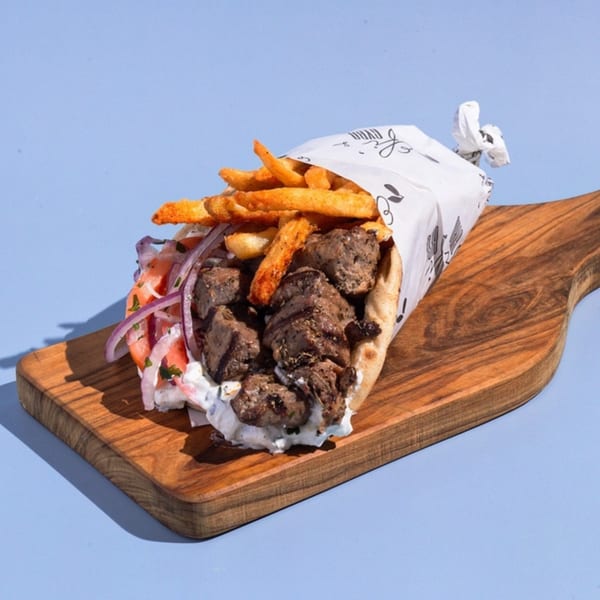 Efi's Gyro with meat, tzatziki, red onions, tomatoes, and fries, wrapped in paper on a wooden board.