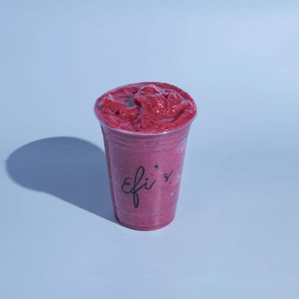 A vibrant red berry smoothie in a clear cup with "Efi's" logo, casting a shadow on a light blue surface.