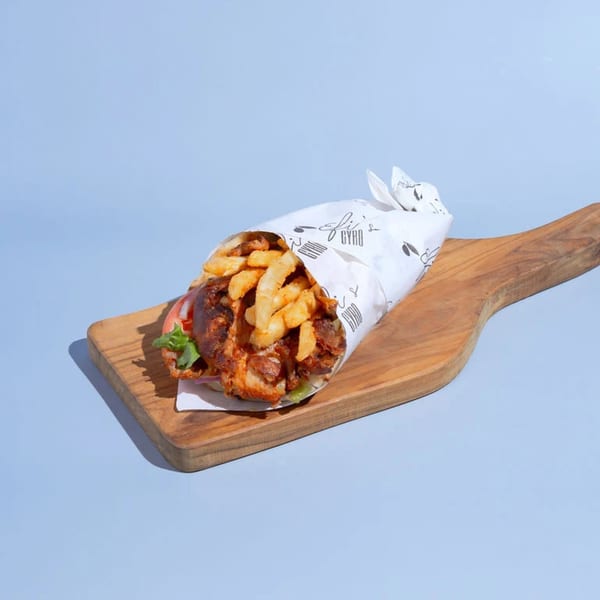 Efi's Gyro, a Greek gyro wrapped in branded paper, filled with meat and fries, on a wooden board.