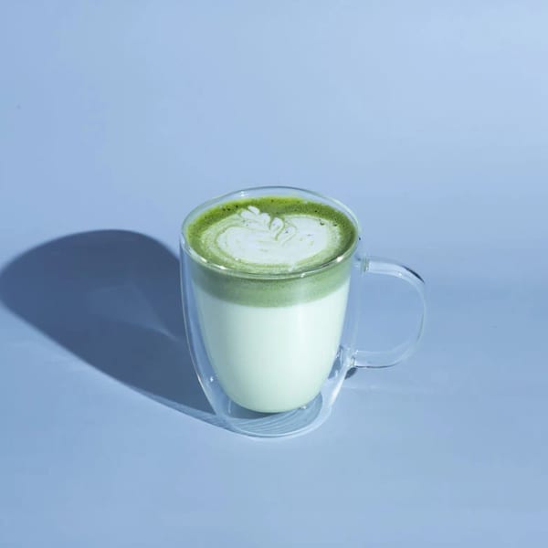 Matcha latte with latte art in a clear glass mug on a light blue background.