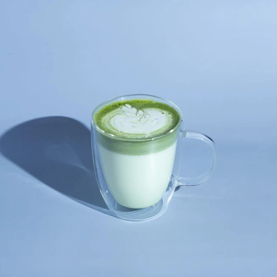 Matcha latte with latte art in a clear glass mug on a light blue background.