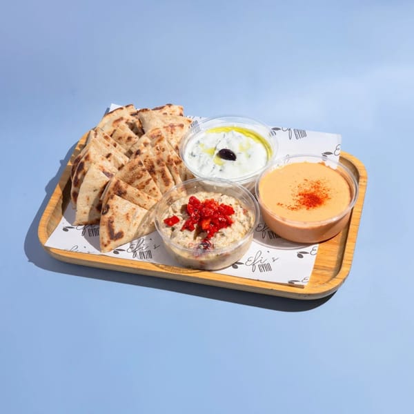 Efi's Gyro platter with pita bread, tzatziki, baba ghanoush, and hummus on a wooden tray.