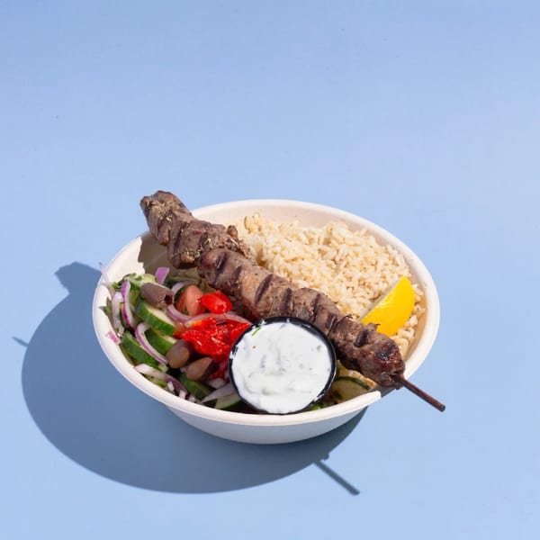 Efi's Gyro bowl with a grilled meat skewer, rice, salad, tzatziki, and lemon wedge.