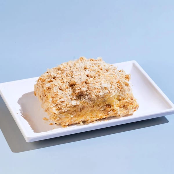 A slice of Napoleon cake with flaky pastry and cream filling on a white rectangular plate.